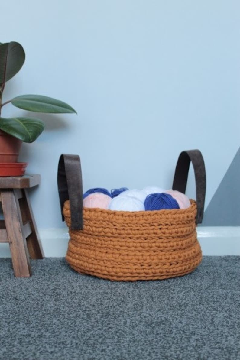 May include: A brown crocheted basket with two dark brown leather handles filled with colorful yarn balls.