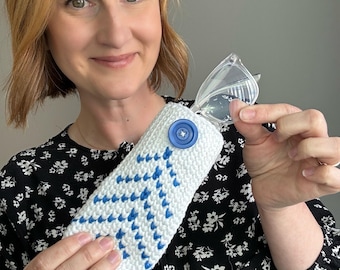 May include: A white and blue knitted glasses case with a large blue button closure. The case has a geometric pattern and is holding a pair of clear eyeglasses.