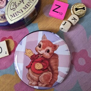 Könnte beinhalten: Ein runder Button mit einem Cartoon-Eichhörnchen in einer roten Jacke, vor einem Union Jack-Hintergrund. Weitere Artikel sind eine Vintage-Dose, Scrabble-Steine und ein kleiner goldfarbener Knopf mit Knochenmuster.