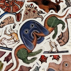K&ouml;nnte beinhalten: Eine Sammlung bunter Aufkleber mit verschiedenen mittelalterlichen Kreaturen und Illustrationen. Die Aufkleber sind auf wei&szlig;em Papier gedruckt und haben eine gl&auml;nzende Oberfl&auml;che. Die Aufkleber beinhalten eine blaue und gr&uuml;ne Kreatur mit einem langen Schwanz, ein braunes Schwein, eine Katze, eine Schnecke und einen Vogel.