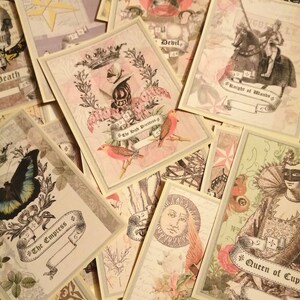 May include: A collection of vintage tarot cards with illustrations of various symbols and characters. The cards are printed on a cream-colored background with gold accents. The cards include "The Empress", "The High Priestess", "The Lovers", "Knight of Wands", "Queen of Cups", "Sun", "Death", "Devil", and "Temperance".