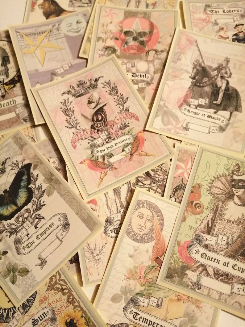 May include: A collection of vintage tarot cards with illustrations of various symbols and characters. The cards are printed on a cream-colored background with gold accents. The cards include "The Empress", "The High Priestess", "The Lovers", "Knight of Wands", "Queen of Cups", "Sun", "Death", "Devil", and "Temperance".