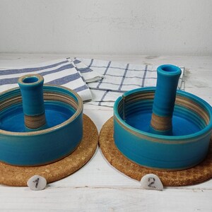 May include: Two teal blue ceramic candle holders with a brown center ring and a brown base. The candle holders are on a cork coaster.