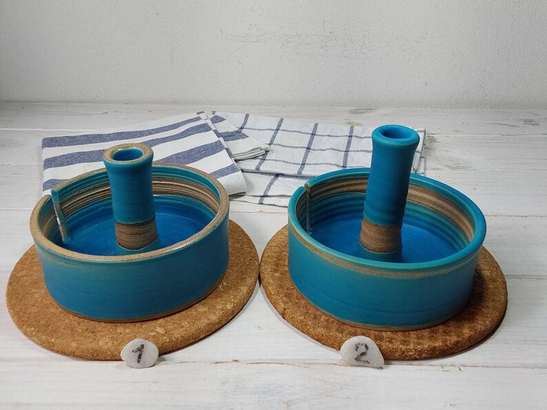 May include: Two teal blue ceramic candle holders with a brown center ring and a brown base. The candle holders are on a cork coaster.