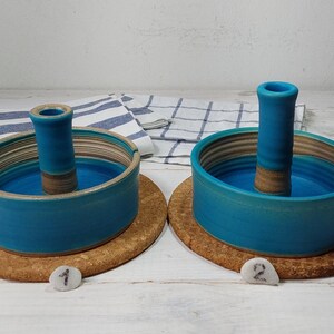 May include: Two teal blue ceramic dish holders with a center stand. The dishes are on a cork base. The dishes are numbered 1 and 2.