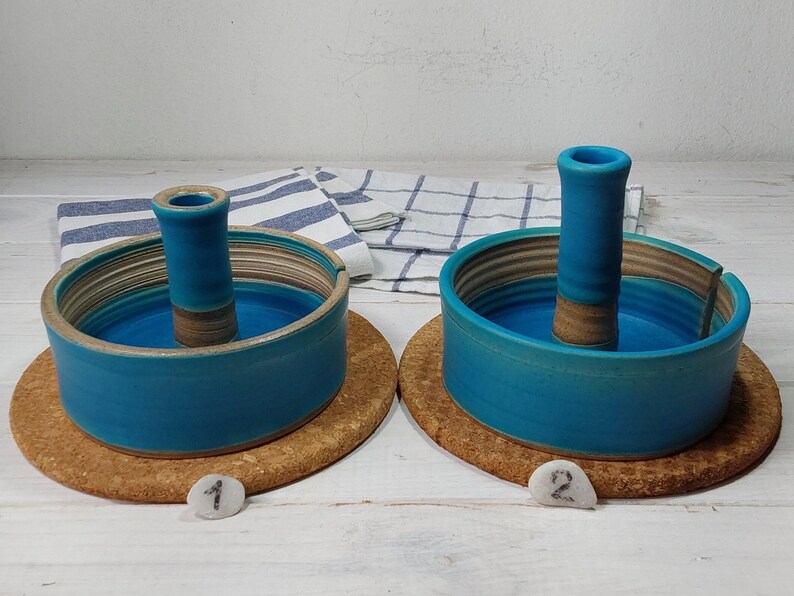 May include: Two teal blue ceramic dish holders with a center stand. The dishes are on a cork base. The dishes are numbered 1 and 2.