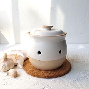 Recipiente de cerámica blanca para guardar ajos, contenedor de almacenamiento de ajos blanco y beige.