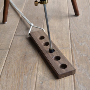 Puede incluir: Una bandeja de madera con seis agujeros para guardar objetos pequeños, como tapones de botella. Una varilla de metal se inserta en uno de los agujeros.