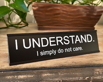 May include: Black desk sign with white text that reads "I understand. I simply do not care."
