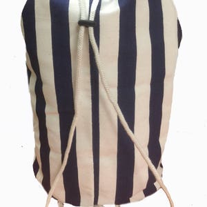 May include: A white and navy blue striped drawstring bag with a white drawstring. The bag is made of canvas and has a simple design.