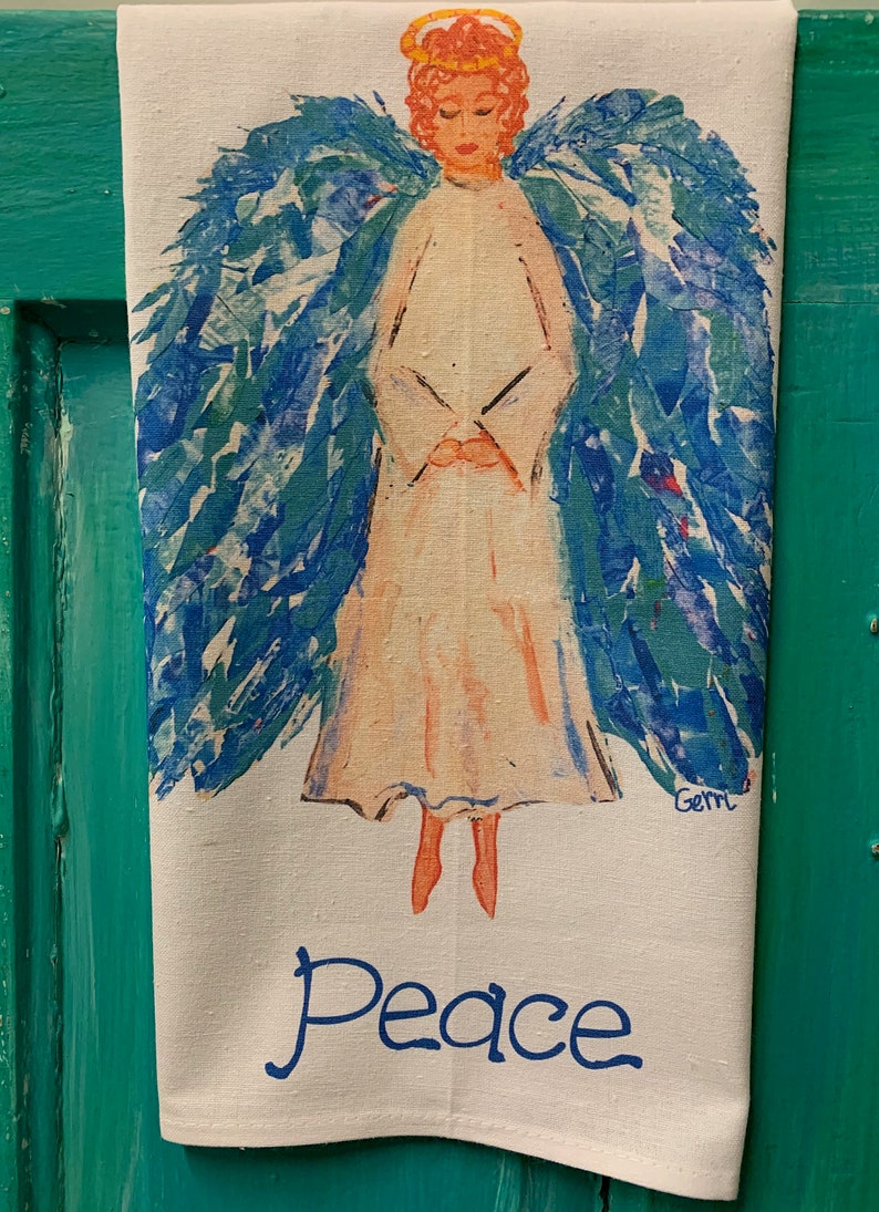 May include: A white tea towel with a blue and green angel painting. The angel has a halo and is holding its hands together. The words "Peace" are written in blue below the angel.