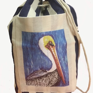 May include: A white and navy blue striped drawstring bag with a pelican illustration on the front. The pelican is painted in shades of brown, yellow, orange, and blue against a blue background.