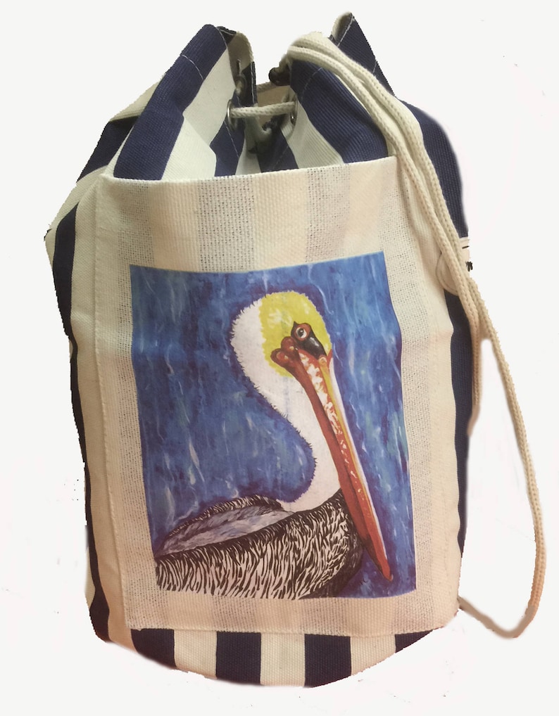 May include: A white and navy blue striped drawstring bag with a pelican illustration on the front. The pelican is painted in shades of brown, yellow, orange, and blue against a blue background.
