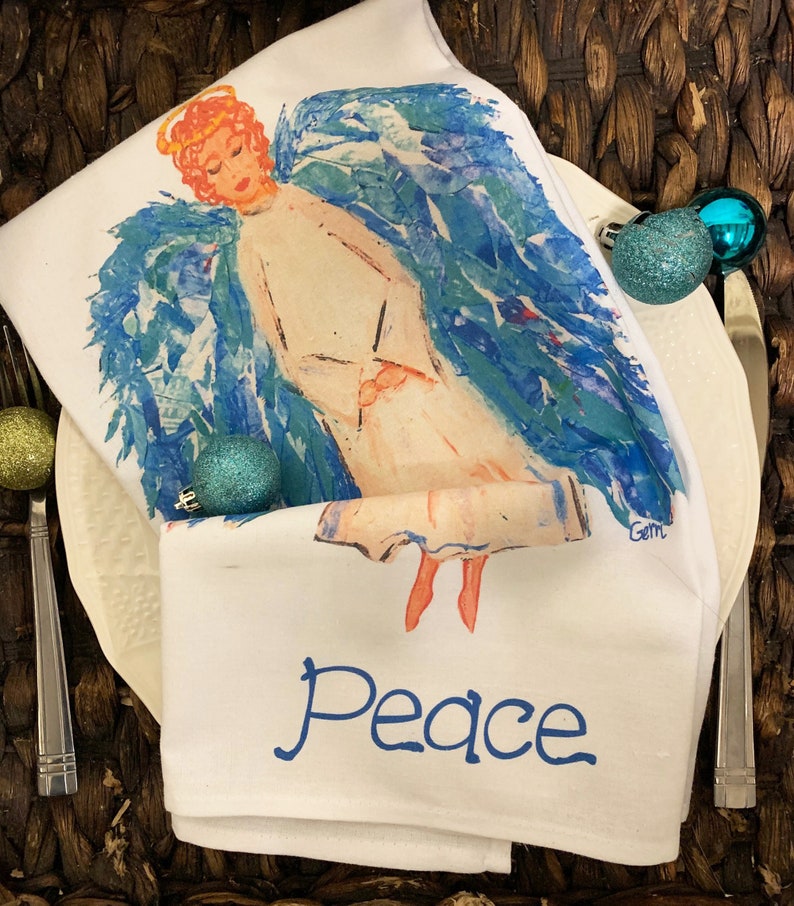 May include: White kitchen towel with a watercolor painting of an angel with blue wings and the word "Peace" printed in blue below the angel.