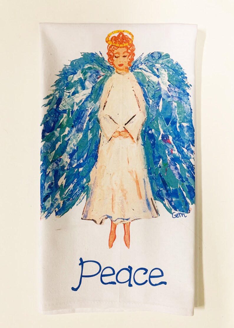 May include: White kitchen towel with a blue and green angel illustration and the word "Peace" in blue lettering. The angel has a halo and is painted in a whimsical style.