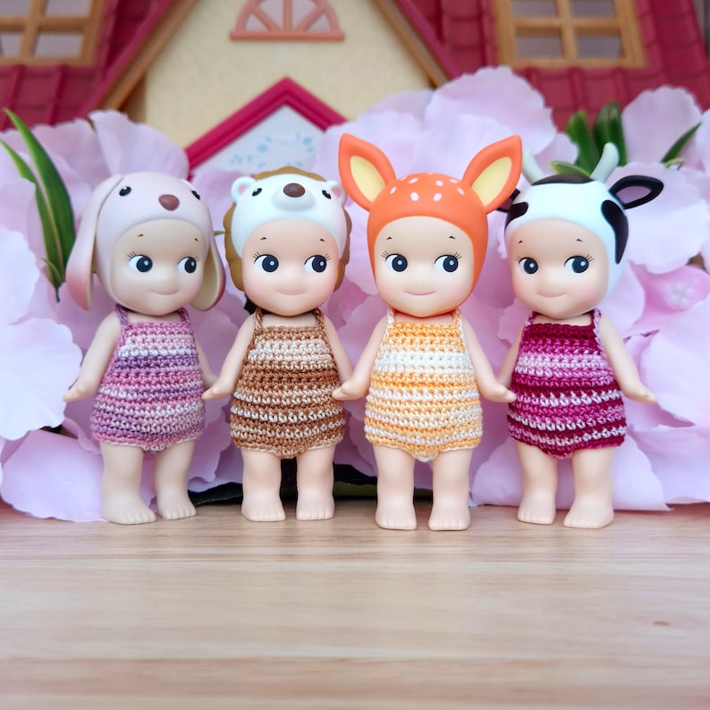 Puede incluir: Cuatro peque&ntilde;as mu&ntilde;ecas que llevan trajes de ba&ntilde;o de ganchillo y sombreros de animales. Las mu&ntilde;ecas llevan trajes de ba&ntilde;o de color rosa, marr&oacute;n, amarillo y rojo. Los sombreros son un conejito, un oso, un ciervo y una vaca.