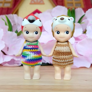 Puede incluir: Dos mu&ntilde;ecas peque&ntilde;as con trajes de ba&ntilde;o y sombreros de ganchillo. La mu&ntilde;eca de la izquierda lleva un traje de ba&ntilde;o de ganchillo de arco&iacute;ris y un sombrero de loro rojo, amarillo y azul. La mu&ntilde;eca de la derecha lleva un traje de ba&ntilde;o de ganchillo marr&oacute;n y un sombrero de oso blanco.