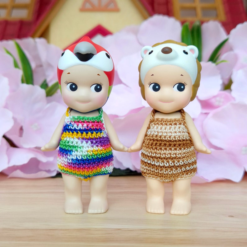Puede incluir: Dos mu&ntilde;ecas peque&ntilde;as con trajes de ba&ntilde;o y sombreros de ganchillo. La mu&ntilde;eca de la izquierda lleva un traje de ba&ntilde;o de ganchillo de arco&iacute;ris y un sombrero de loro rojo, amarillo y azul. La mu&ntilde;eca de la derecha lleva un traje de ba&ntilde;o de ganchillo marr&oacute;n y un sombrero de oso blanco.