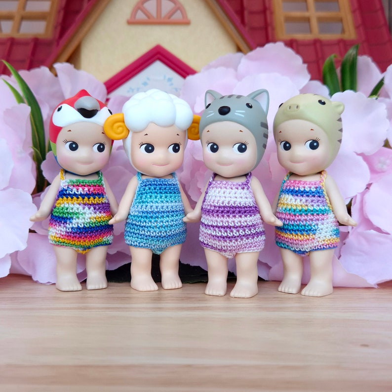 Puede incluir: Cuatro peque&ntilde;as mu&ntilde;ecas que llevan trajes de ba&ntilde;o de ganchillo y sombreros de animales. Las mu&ntilde;ecas est&aacute;n de pie sobre una superficie de madera. Las mu&ntilde;ecas llevan una variedad de colores, incluyendo arco&iacute;ris, azul, morado y verde.