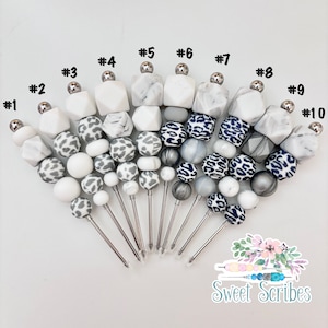 以下が含まれることがあります： 異なる色のビーズが付いた銀製の串が10本。ビーズは白、グレー、黒で、ヒョウ柄です。串は1から10まで番号が付けられています。