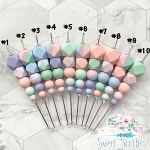 Peut inclure: Dix marqueurs de point en fil métallique et perles géométriques marbrées de couleurs. Les perles sont dans des tons de rose, vert et violet. Les marqueurs de point sont numérotés de 1 à 10.