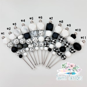 以下が含まれることがあります： 銀色のアクセントが付いた、黒と白のシリコンビーズネックレスが11本。各ネックレスは、大理石、音楽記号、ギンガムチェックなど、さまざまなビーズの組み合わせが特徴です。