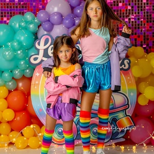 May include: Two girls wearing colorful outfits and rainbow striped knee-high socks pose in front of a backdrop with balloons and a roller skate graphic. The backdrop has the text "Let's Roll" on it.