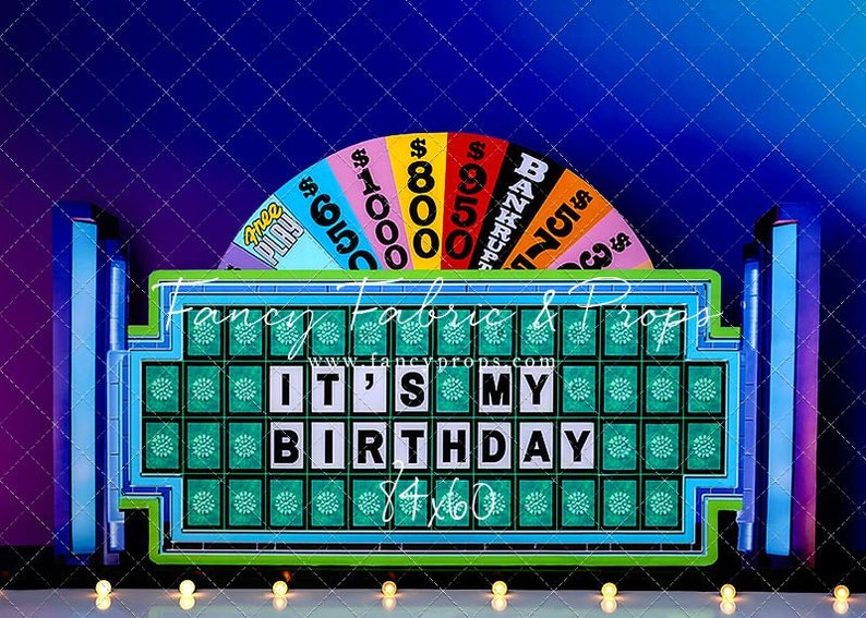 May include: A blue and green game show board with the text "IT'S MY BIRTHDAY" on it. The board is surrounded by a colorful wheel with dollar amounts and the word "BANKRUPT".