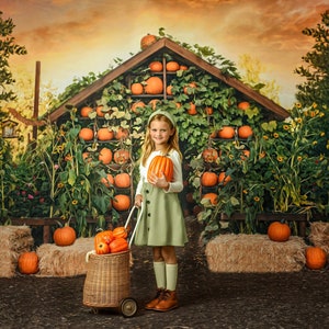 May include: A young person in a green dress and headband holds an orange pumpkin, standing in front of a pumpkin-filled shed. A wicker basket on wheels is filled with pumpkins. Hay bales and sunflowers are in the background, creating a fall harvest scene.