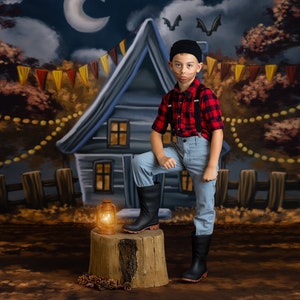 May include: A young person dressed as a lumberjack stands on a tree stump in front of a painted backdrop. The backdrop depicts a house with a fence, trees, and a crescent moon. The person is wearing a red and black plaid shirt, blue jeans, black boots, and a black beanie. A lantern sits on the stump.