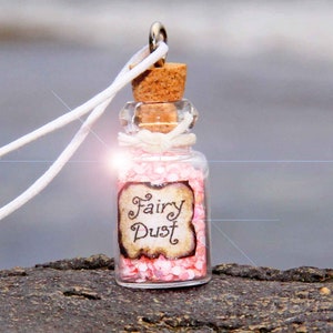 Könnte beinhalten: Eine kleine Glasflasche mit einem Korkverschluss und einer weißen Schnur, die um den Hals gebunden ist. Die Flasche ist mit rosa Glitzer gefüllt und trägt ein Etikett mit der Aufschrift "Fairy Dust".