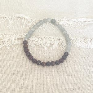 May include: A beaded bracelet featuring a mix of dark red and gray-blue gemstones. The bracelet is made of small, round beads strung together, creating a simple yet elegant accessory. The beads are arranged in a gradient, transitioning from dark to light.