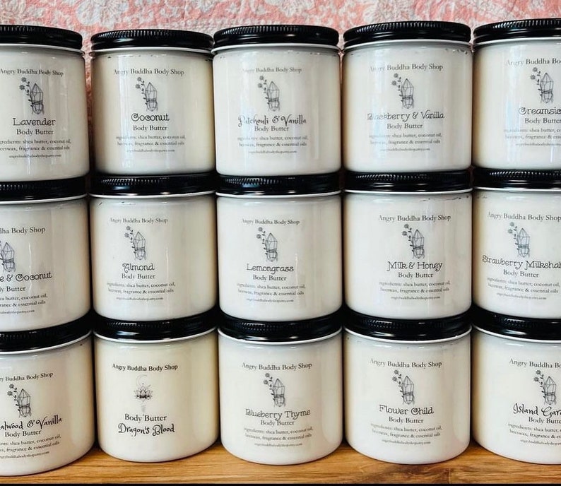 May include: A collection of 12 white jars with black lids and labels. Each jar contains body butter with a different scent. The scents are Lavender, Coconut, Patchouli & Vanilla, Raspberry & Vanilla, Dreamsicle, Almond, Lemongrass, Milk & Honey, Strawberry Milkshake, Sandalwood & Vanilla, Dragon's Blood, Blueberry Thyme, Flower Child, and Island Garden.