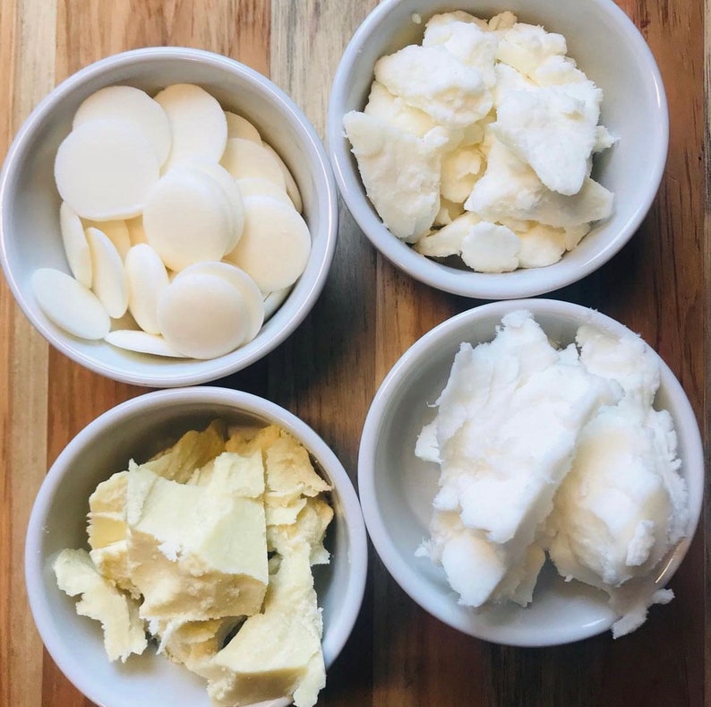 May include: Four white bowls, each containing a different type of white, solid, unrefined fat. The bowls are arranged in a square on a wooden surface.