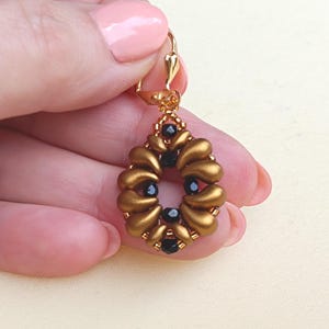 May include: A drop earring featuring a central oval arrangement of matte bronze-colored petal-shaped beads accented with small, faceted black beads. The earring is attached to a gold-toned metal lever-back finding at the top.
