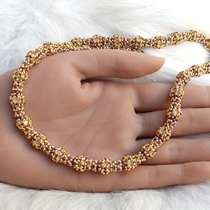 May include: A beaded necklace constructed from small, metallic gold and deep red seed beads arranged in a repeating, textured spherical pattern. The circular chain features a consistent, intricate woven design throughout its entire length.