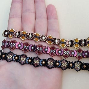 May include: Three beaded bracelets in shades of brown, burgundy, and black. Each bracelet features a repeating geometric pattern with small beads and accents. The bracelets are displayed on a light background.