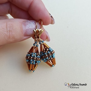 以下が含まれることがあります： 手作りのビーズイヤリングのペア。イヤリングは金色のフックと涙の形をしたデザインが特徴です。涙の形は茶色、青、金色のビーズで作られています。イヤリングは手で持たれています。