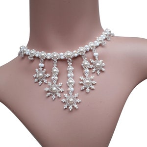 May include: A white beaded necklace with snowflake pendants. The necklace is made with small white beads and features five snowflake-shaped pendants.