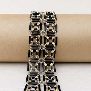 Peut inclure: Un bracelet tissé présentant un motif géométrique de longues perles cylindriques noires disposées en colonnes verticales, reliées par de petites perles rondes métalliques dorées et argentées formant une grille carrée répétitive.