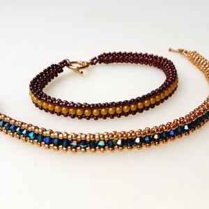 May include: Two beaded bracelets, one with gold and blue beads and the other with burgundy and gold beads.