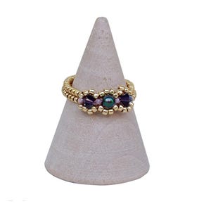 May include: A gold ring with a beaded design and purple and green stones.