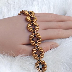 May include: A gold-colored beaded bracelet with a floral design. The bracelet features a series of connected flower-shaped beads, each with a dark center. The bracelet is displayed on a white, fluffy surface.