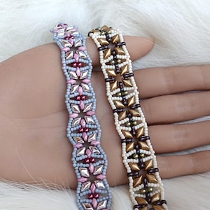 Könnte beinhalten: Zwei Perlenarmbänder mit komplexen Webmustern. Das linke Armband besteht aus hellblauen, rosafarbenen und metallisch silbernen Perlen. Das rechte Armband zeigt cremefarbene, dunkelbraune und metallisch goldene Perlen in geometrischem Design.