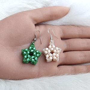 May include: A pair of star-shaped dangle earrings crafted from small beads. One earring is a vibrant emerald green, while the other is a soft cream color. Both earrings feature silver-toned metal hooks for attachment and a faceted bead texture.