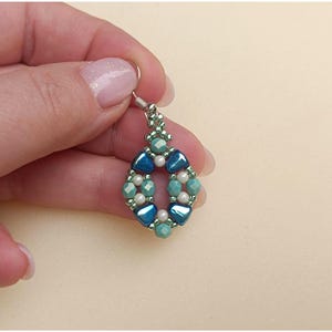 May include: A dangle earring featuring a diamond-shaped arrangement of beads. The design incorporates metallic blue triangular beads, faceted light blue beads, and small white round beads, all connected by tiny green seed beads on a silver hook.