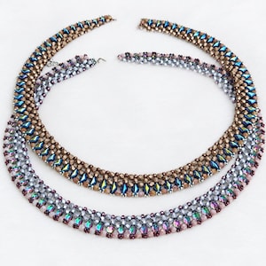 Op de afbeelding: Twee kralenkettingen in een cirkelvormig patroon. De bovenste ketting heeft bronzen en iriserend blauwe ruitvormige kralen. De onderste ketting bestaat uit zilveren, iriserend paarse en roze kralen met een geweven, meerstrengs structuur.
