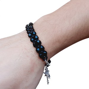 May include: A black beaded bracelet with a silver charm. The bracelet is made of small, faceted beads and has a delicate silver chain with a charm at the end.