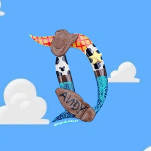 Op de afbeelding: Een grillige, gestileerde letter "D" met een cowboythema tegen een blauwe lucht met wolken. Het ontwerp bevat een bruine cowboyhoed, een ster en de naam "Andy" op een laars, met een koeienhuidpatroon.