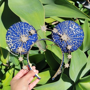 Può includere: Orecchie di Minnie Mouse blu e oro scintillanti con un cerchietto in filo d'oro e decorazioni a forma di stella. Le orecchie sono ricoperte di paillettes e hanno una finitura scintillante.